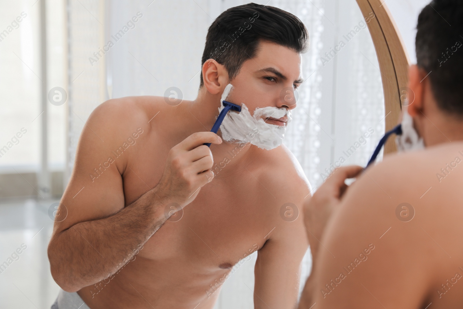 Photo of Handsome man shaving near mirror in bathroom