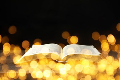 Open Bible on wooden table, bokeh effect