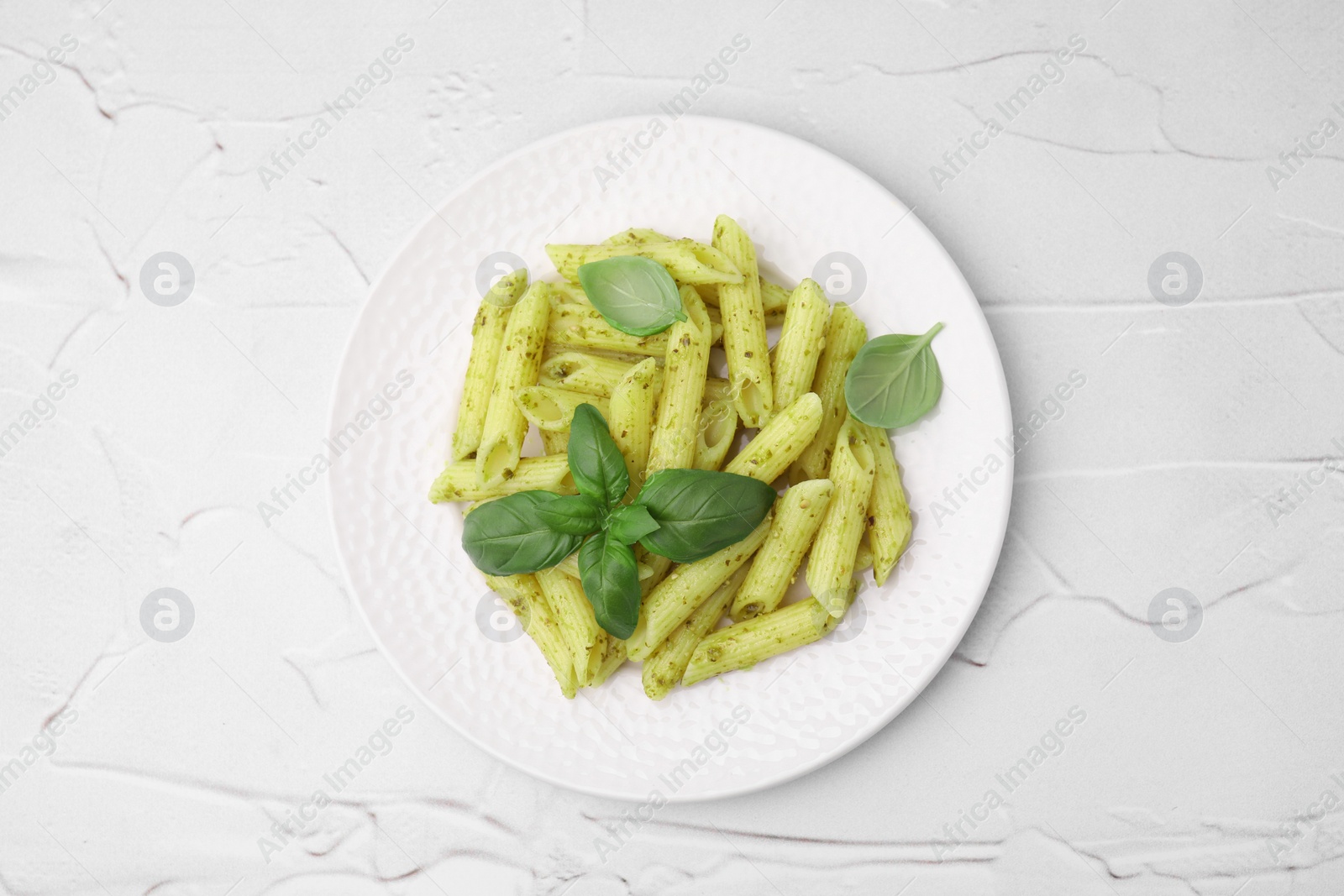 Photo of Delicious pasta with pesto sauce and basil on white textured table, top view