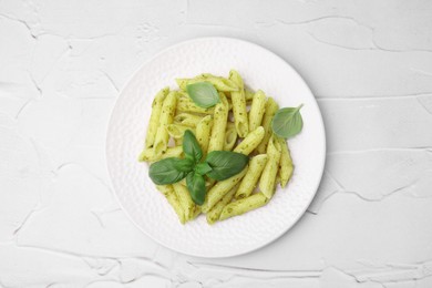 Delicious pasta with pesto sauce and basil on white textured table, top view