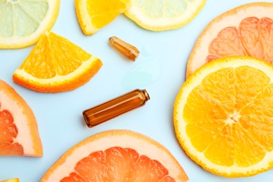 Broken skincare ampoule with vitamin C and slices of different citrus fruits on light blue background, flat lay