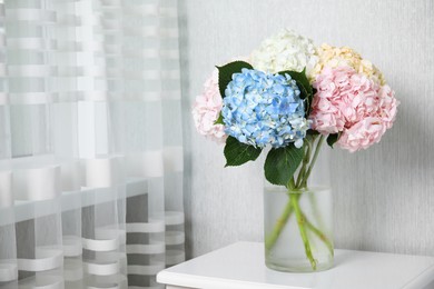 Photo of Beautiful hydrangea flowers in vase on white bedside table indoors, space for text