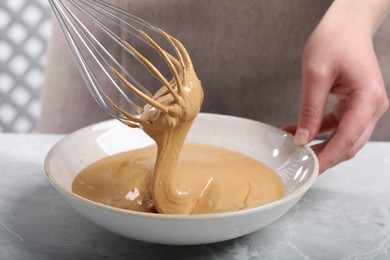 Woman whipping coffee cream at light gray table, closeup