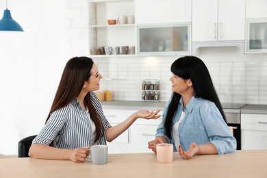 Photo of Young daughter speaking with her mature mother at table indoors