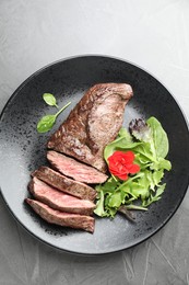Pieces of delicious grilled beef meat and greens on grey table, top view