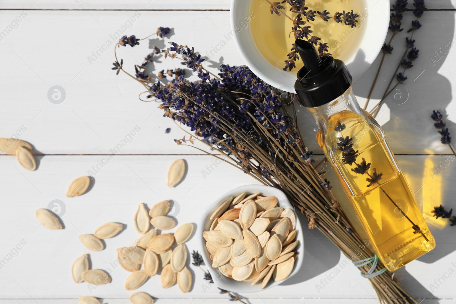 Photo of Healthy cooking oil, lavender flowers and pumpkin seeds on white wooden table, flat lay