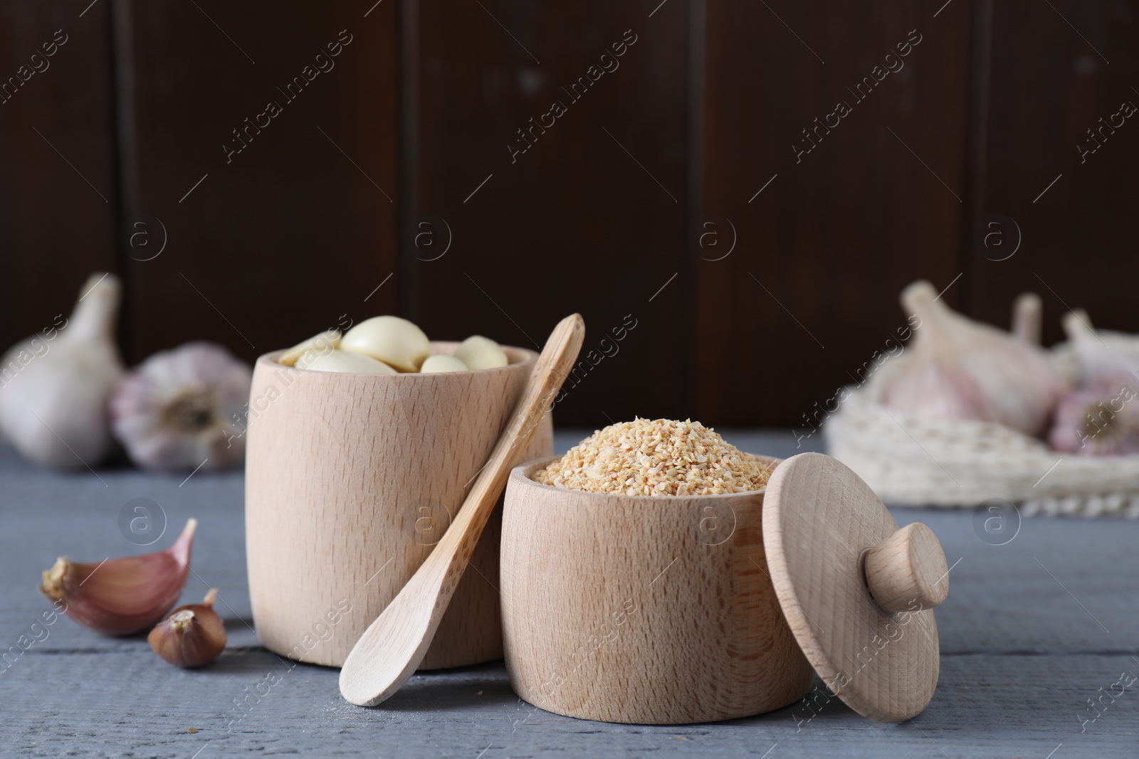 Photo of Dehydrated garlic granules, fresh cloves and spoon on grey wooden table