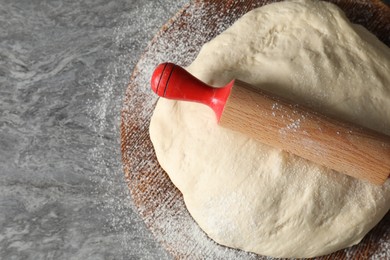 Photo of Raw dough and rolling pin on grey table, top view. Space for text