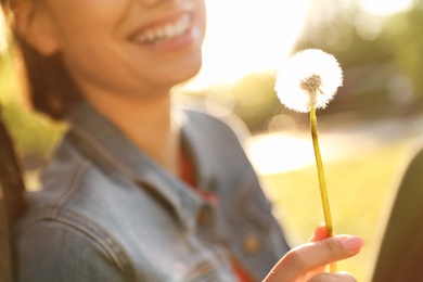 Young woman with dandelion in park on sunny day, closeup. Allergy free concept