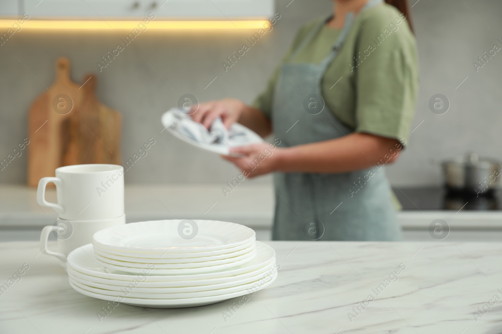 Photo of Woman wiping dish with towel in kitchen, focus on stack of plates