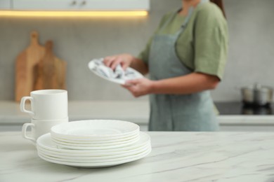 Woman wiping dish with towel in kitchen, focus on stack of plates