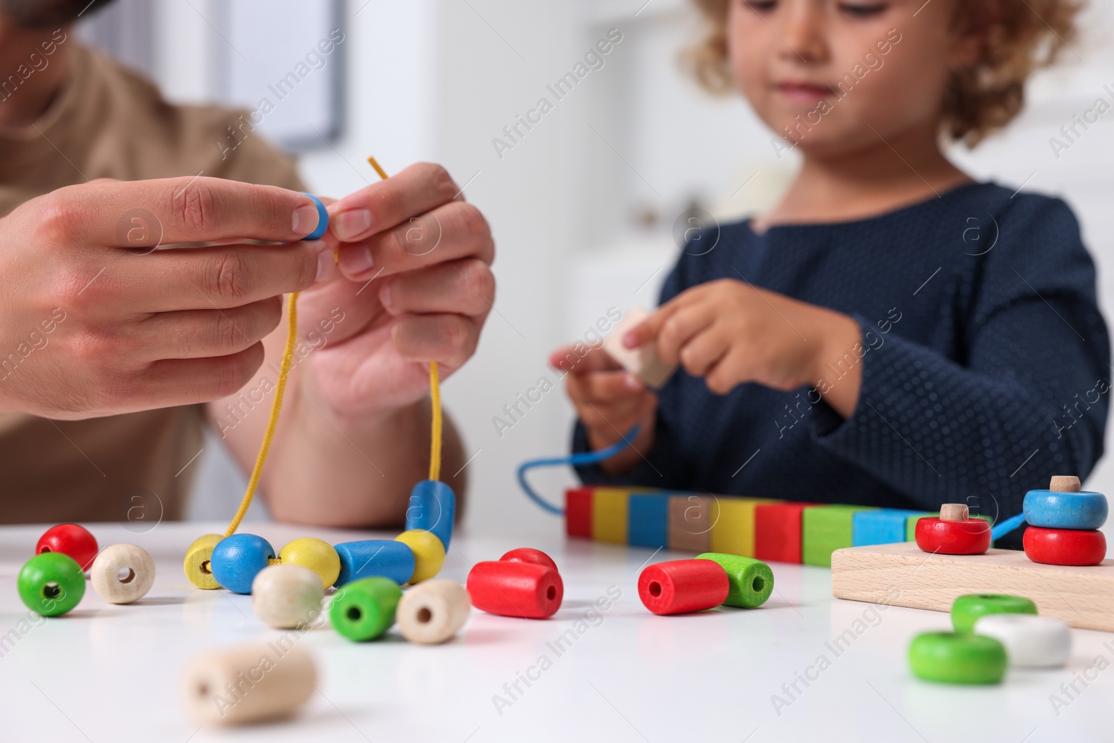 Photo of Motor skills development. Father and daughter playing with wooden pieces and strings for threading activity at table indoors, closeup