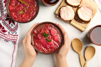 Woman with clay bowl of Ukrainian borsch at table, top view