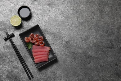 Sashimi set (raw tuna, salmon slices) served with soy sauce and lime on grey table, flat lay. Space for text