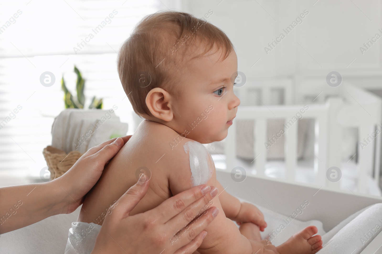 Photo of Mother applying body cream on her little baby at home, closeup