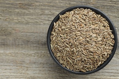 Photo of Bowl of caraway seeds on wooden table, top view. Space for text