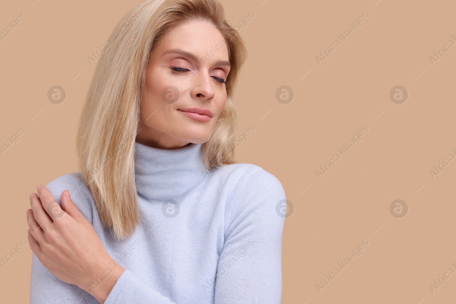 Photo of Portrait of beautiful middle aged woman with blonde hair on beige background. Space for text