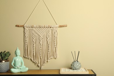 Photo of Beautiful macrame hanging on beige wall in room. Decorative element