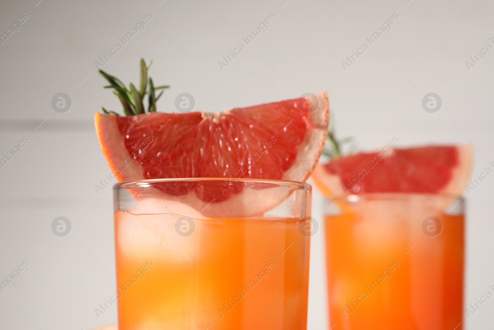 Photo of Tasty grapefruit drink with ice in glasses, rosemary and slices of fresh fruit on white background, closeup