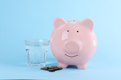 Photo of Water scarcity concept. Piggy bank, glass of drink and coins on light blue background