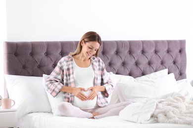 Happy pregnant woman sitting in bed at home