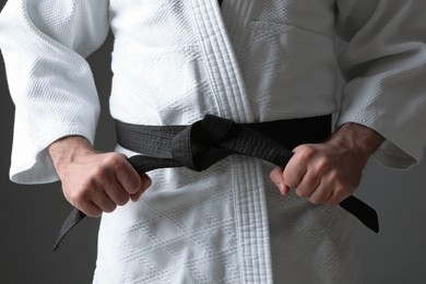 Photo of Karate coach wearing kimono and black belt on grey background, closeup