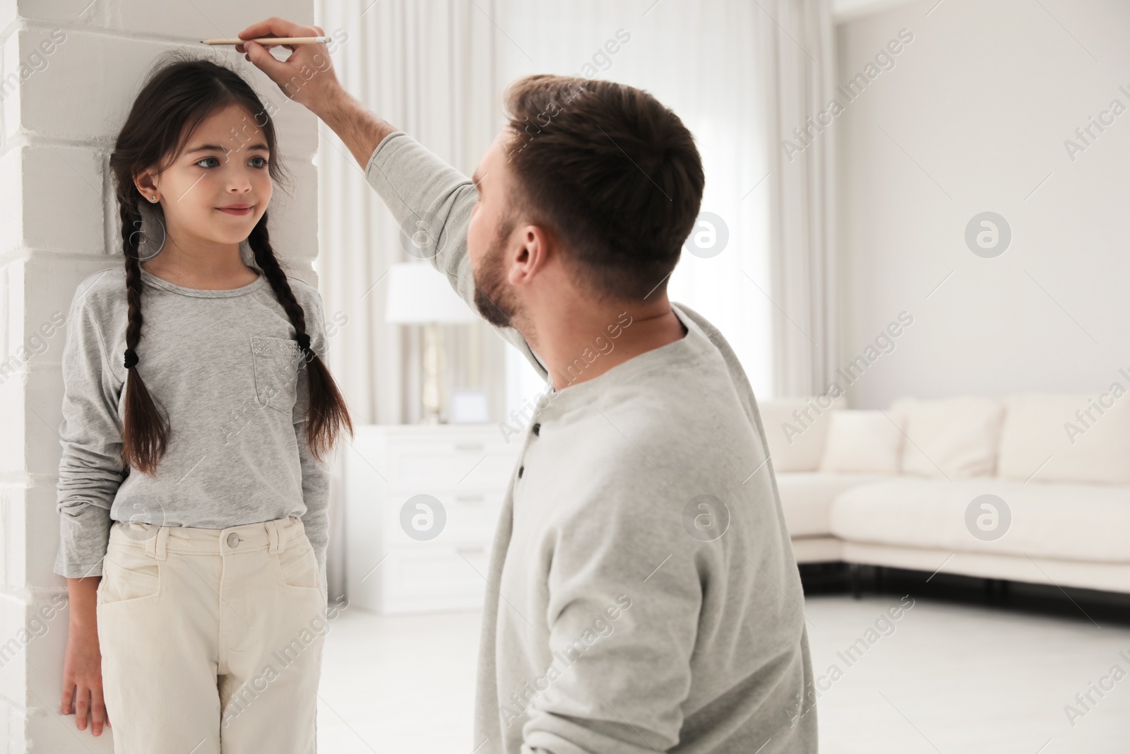 Photo of Father measuring daughter's height near white brick pillar at home