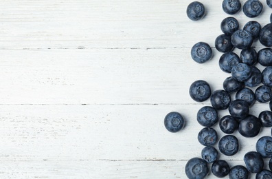Photo of Tasty fresh blueberries on white wooden table, top view with space for text