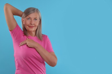 Photo of Beautiful senior woman doing breast self-examination on light blue background, space for text