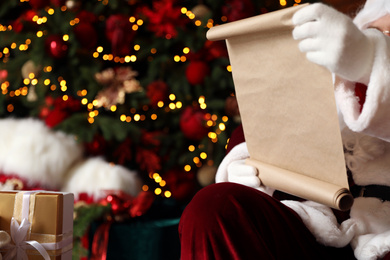 Photo of Santa Claus reading wish list against blurred festive lights, closeup