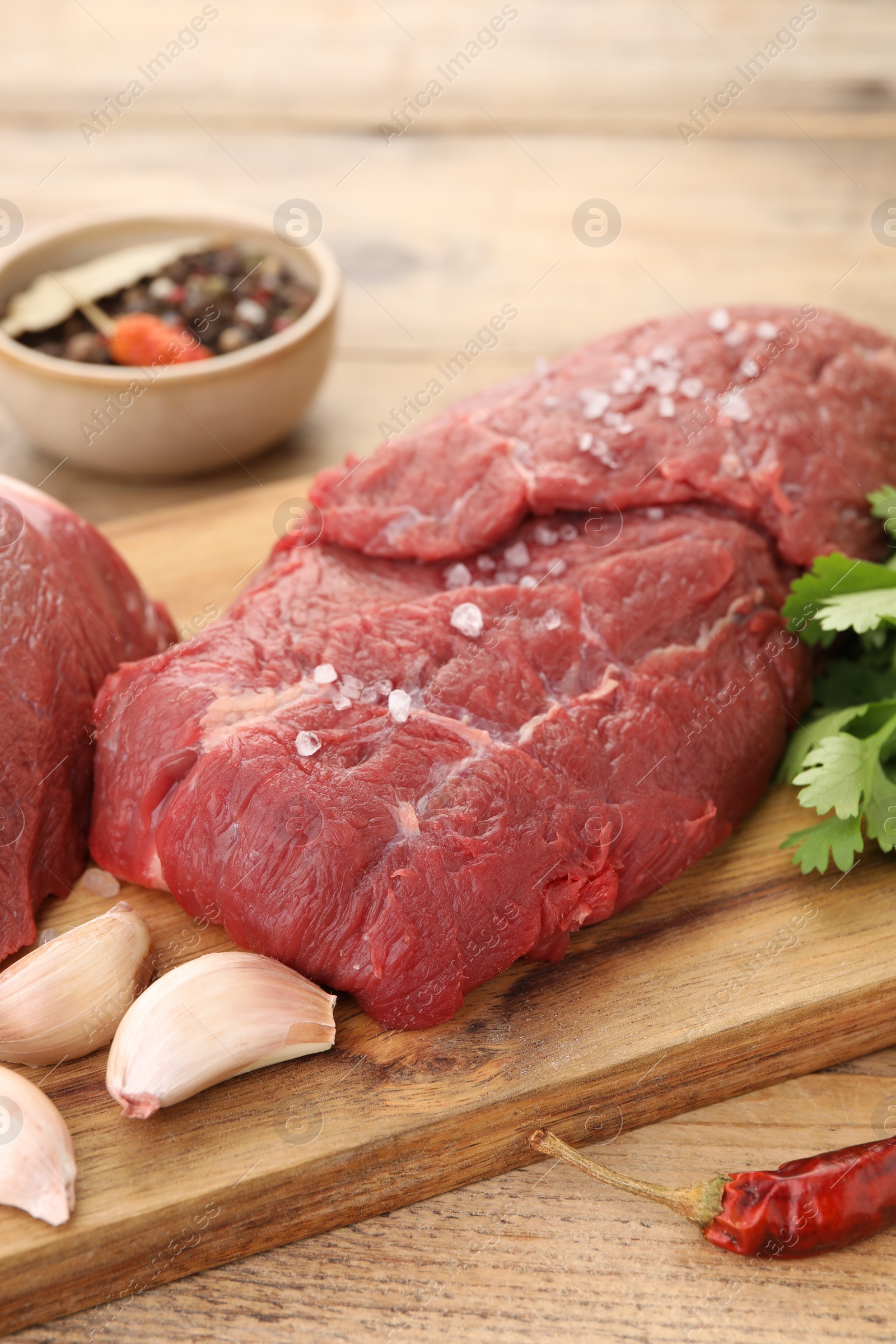 Photo of Pieces of raw beef meat, chili pepper, garlic and spices on wooden table, closeup