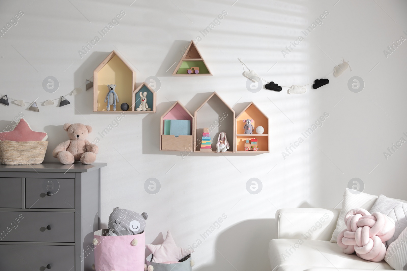 Photo of Cute children's room with house shaped shelves, sofa and chest of drawers. Interior design