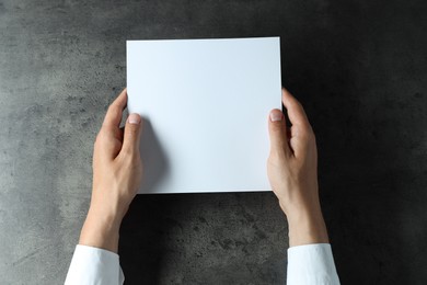 Photo of Man holding blank book at black textured table, top view. Mockup for design