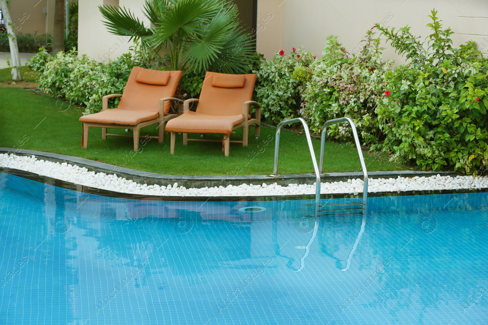 Photo of Sunbeds near modern swimming pool with stairs at resort