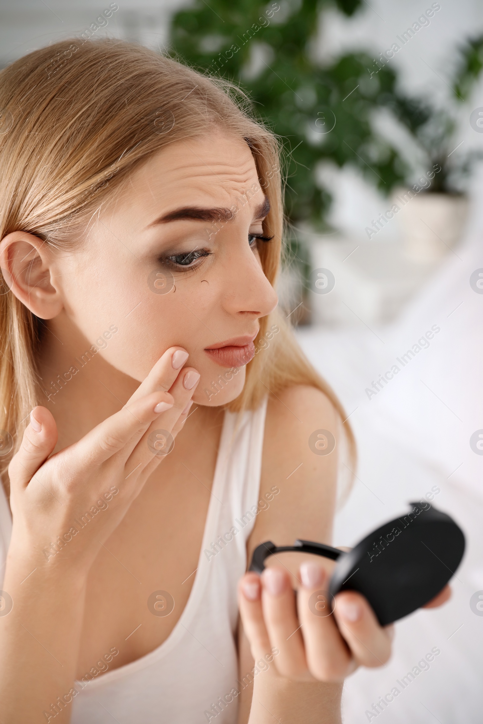 Photo of Young woman with eyelash loss problem looking in mirror indoors