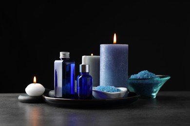 Photo of Spa composition. Cosmetic products, burning candles and sea salt on gray table against black background