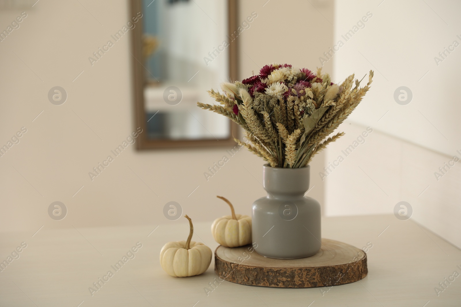 Photo of Beautiful bouquet of dry flowers in vase and small pumpkins on white table indoors, space for text