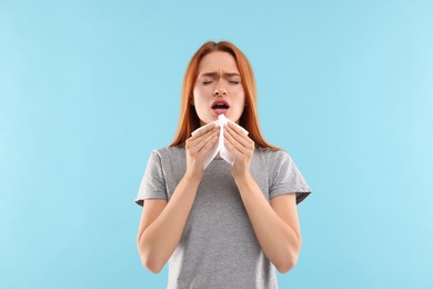 Photo of Suffering from allergy. Young woman with tissue sneezing on light blue background