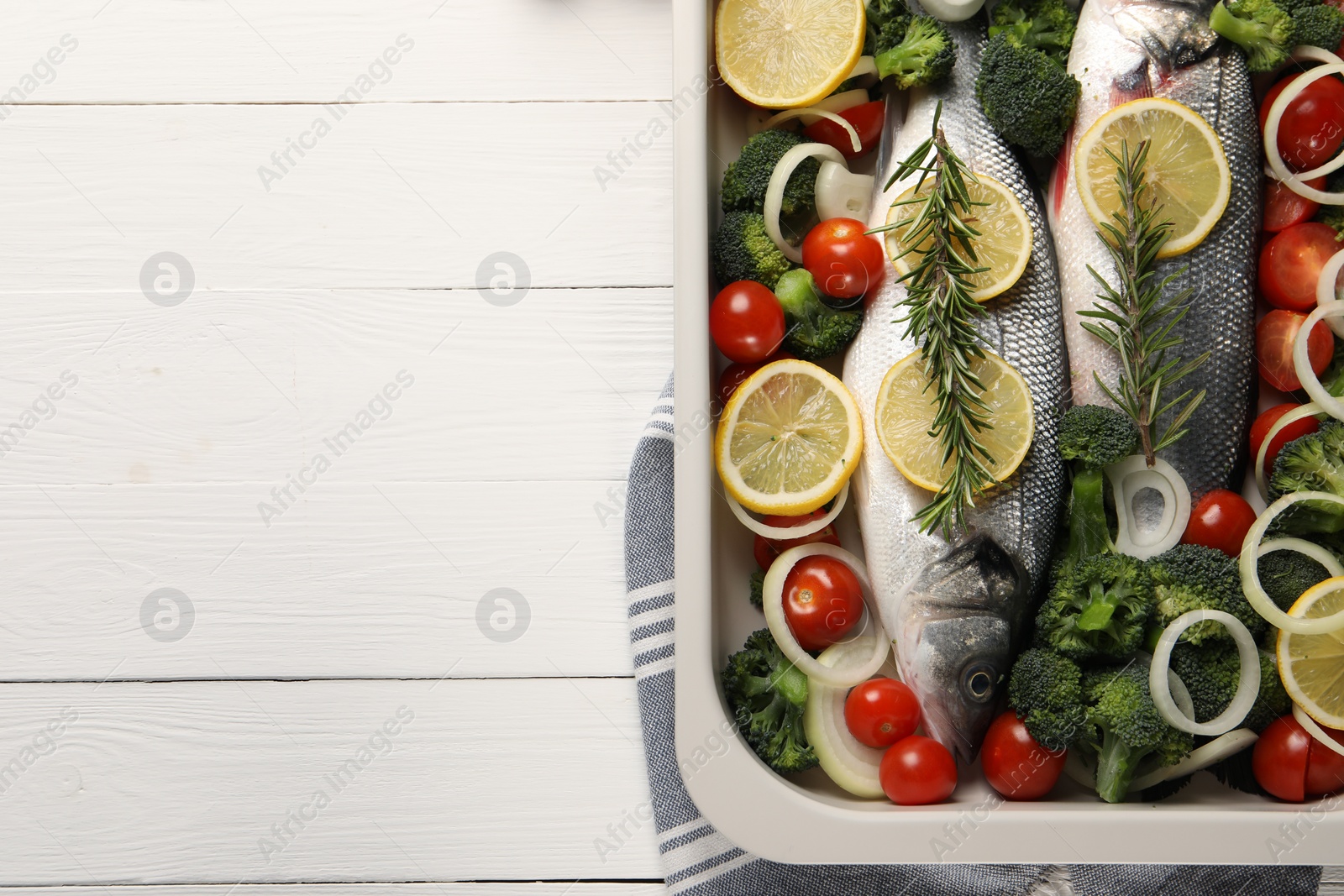 Photo of Raw fish with vegetables and lemon in baking dish on white wooden table, top view. Space for text