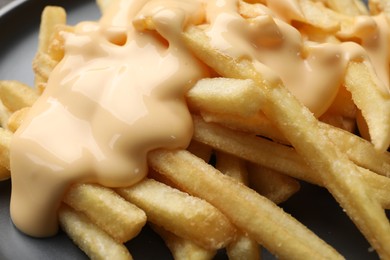 Photo of Delicious french fries with cheese sauce on plate, closeup