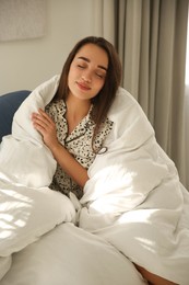 Photo of Beautiful young woman wrapped with soft blanket relaxing on armchair at home