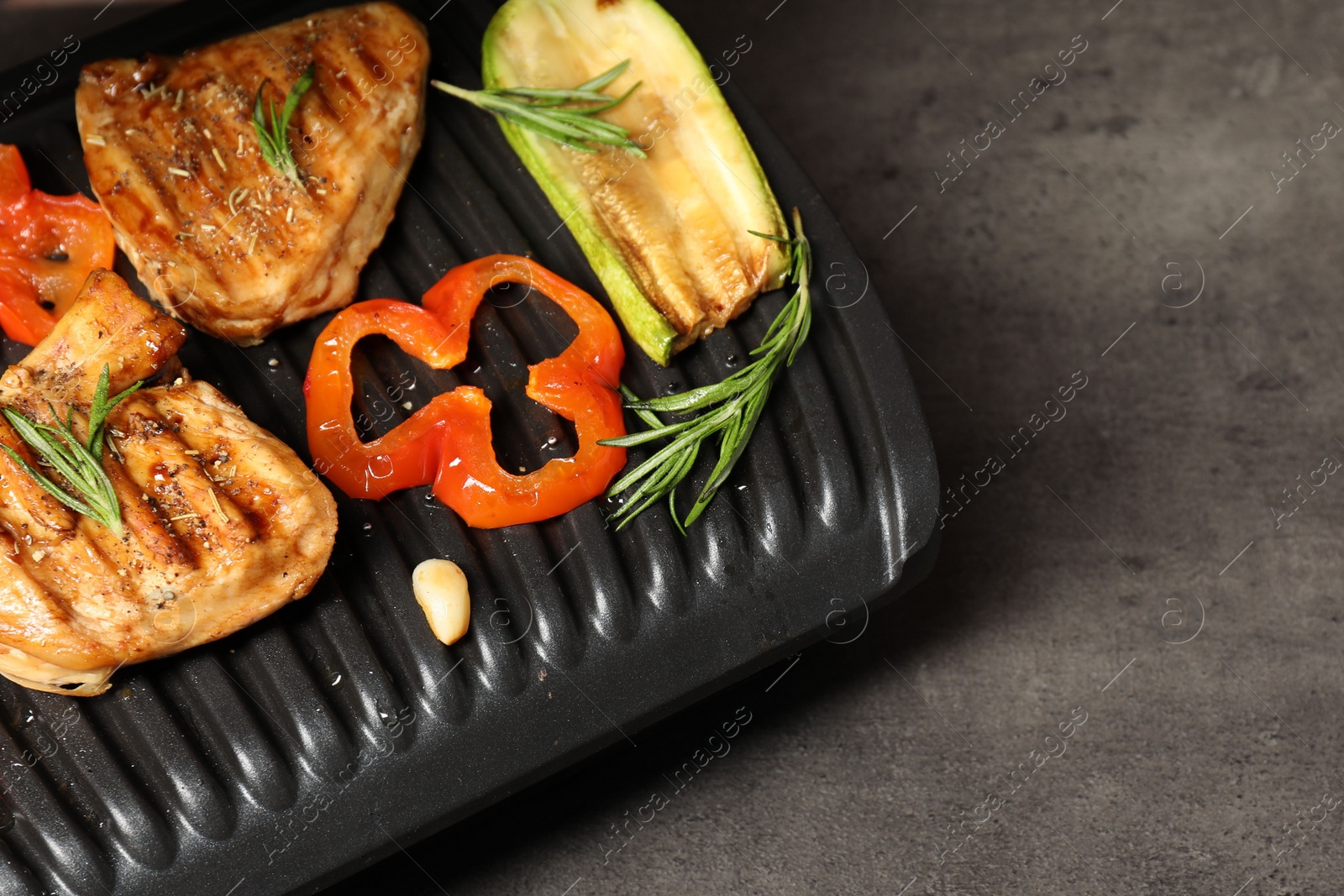 Photo of Electric grill with tasty meat, spices and vegetables on grey textured table, space for text