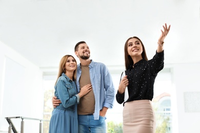 Photo of Female real estate agent showing new house to couple, indoors