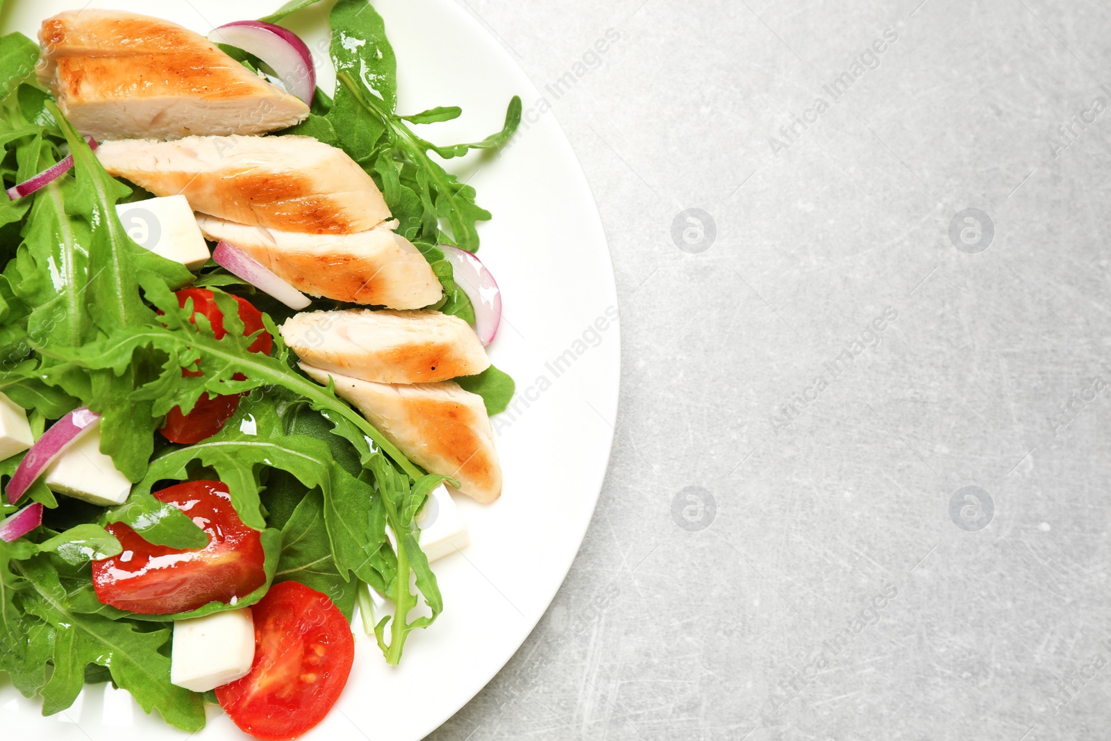 Photo of Delicious salad with meat, arugula and vegetables on grey table, top view