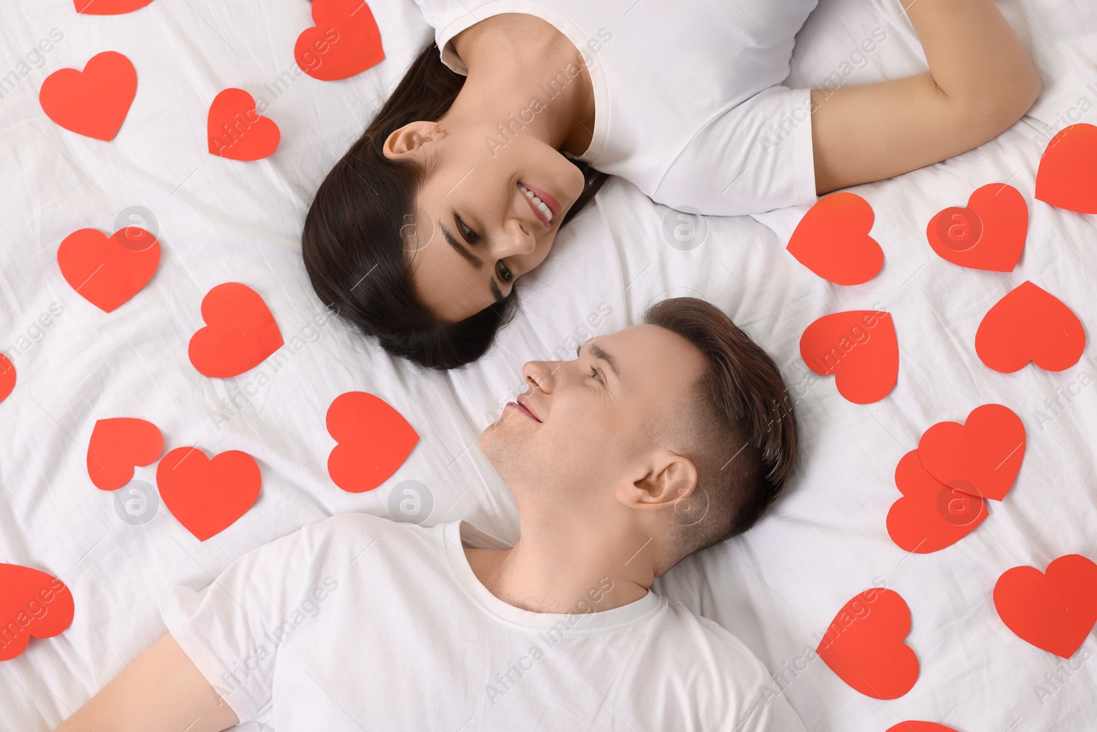 Photo of Lovely couple on bed with many decorative hearts, top view. Valentine's day celebration