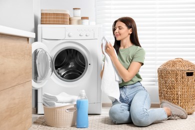 Photo of Woman smelling clean towels near washing machine in bathroom
