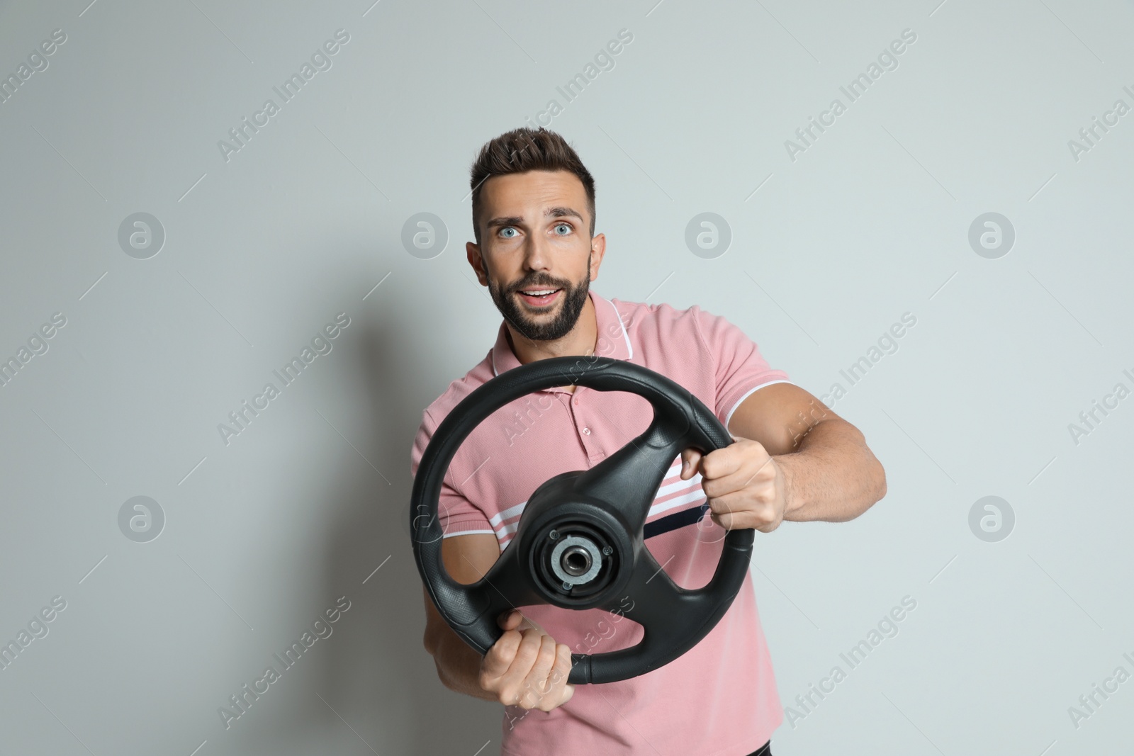 Photo of Happy man with steering wheel on grey background