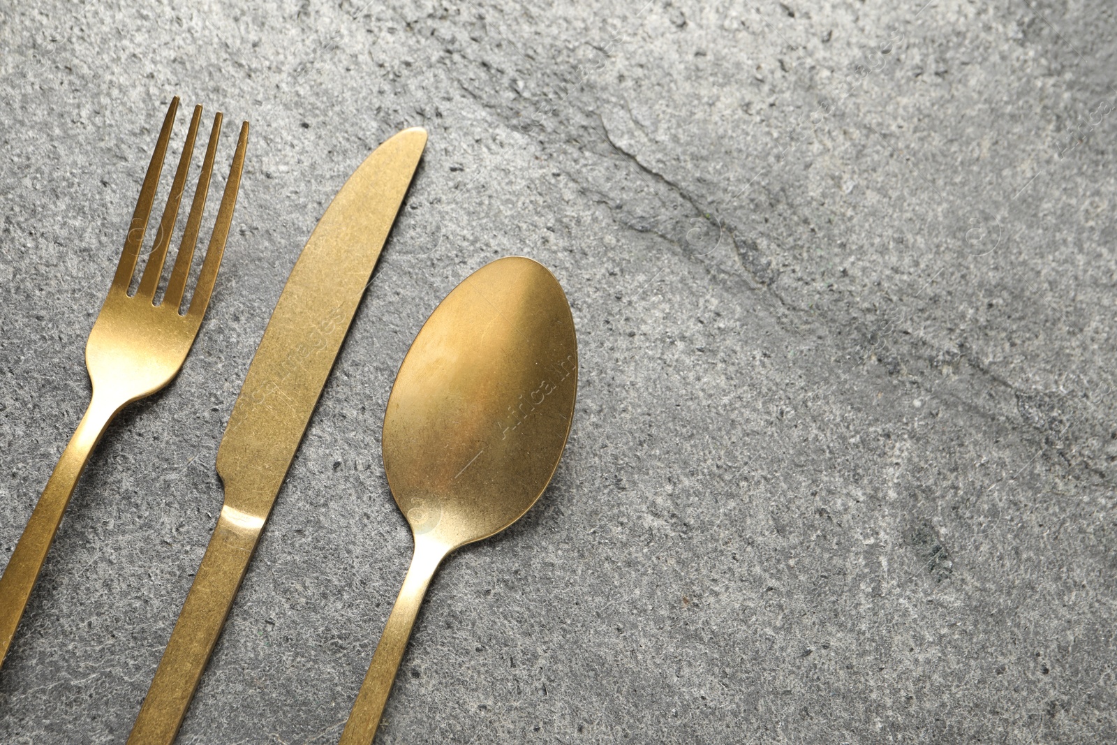 Photo of Stylish golden cutlery on grey table, flat lay. Space for text