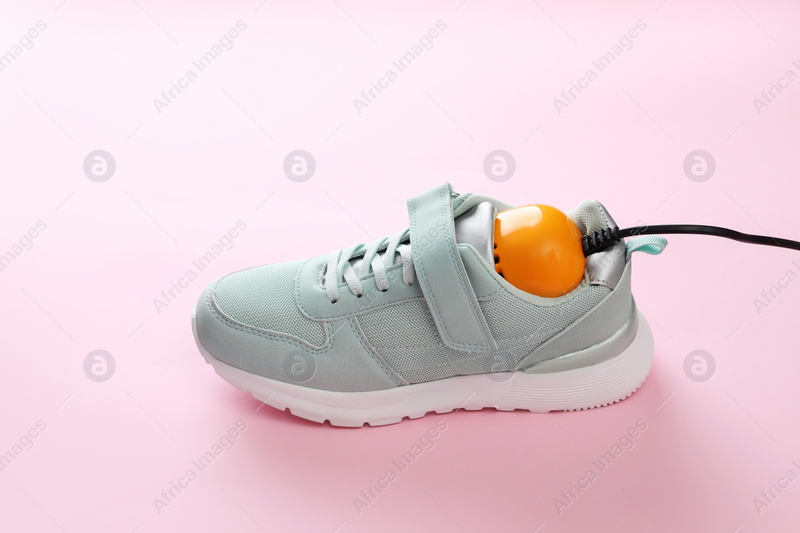 Photo of Stylish sneaker with modern electric shoe dryer on pink background