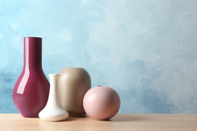 Photo of Stylish ceramic vases on wooden table against light blue background. Space for text